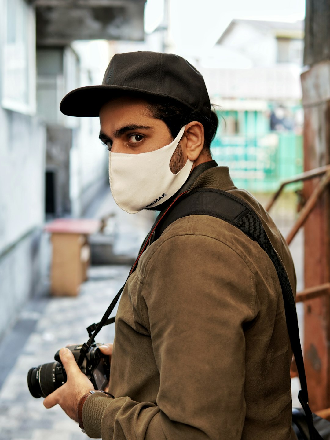 man in brown jacket wearing white mask holding black dslr camera