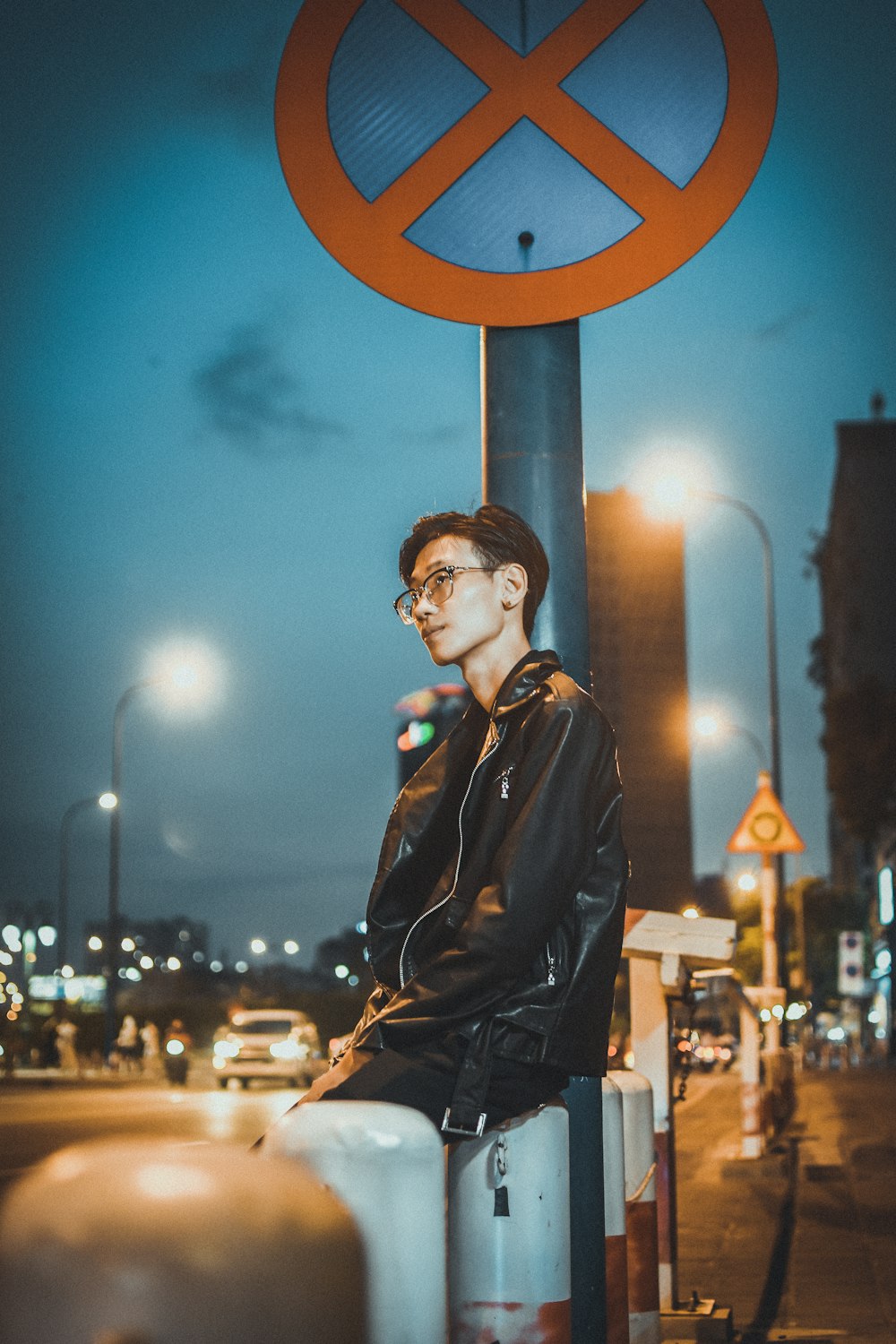 man in black leather jacket standing near brown round metal stand during night time