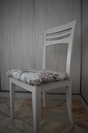 A velvet cushion with a subtle floral pattern resting on a wooden chair.