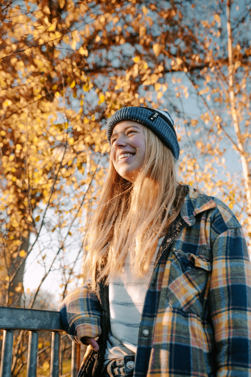 woman in black knit cap and brown and black plaid coat standing near brown leaf tree