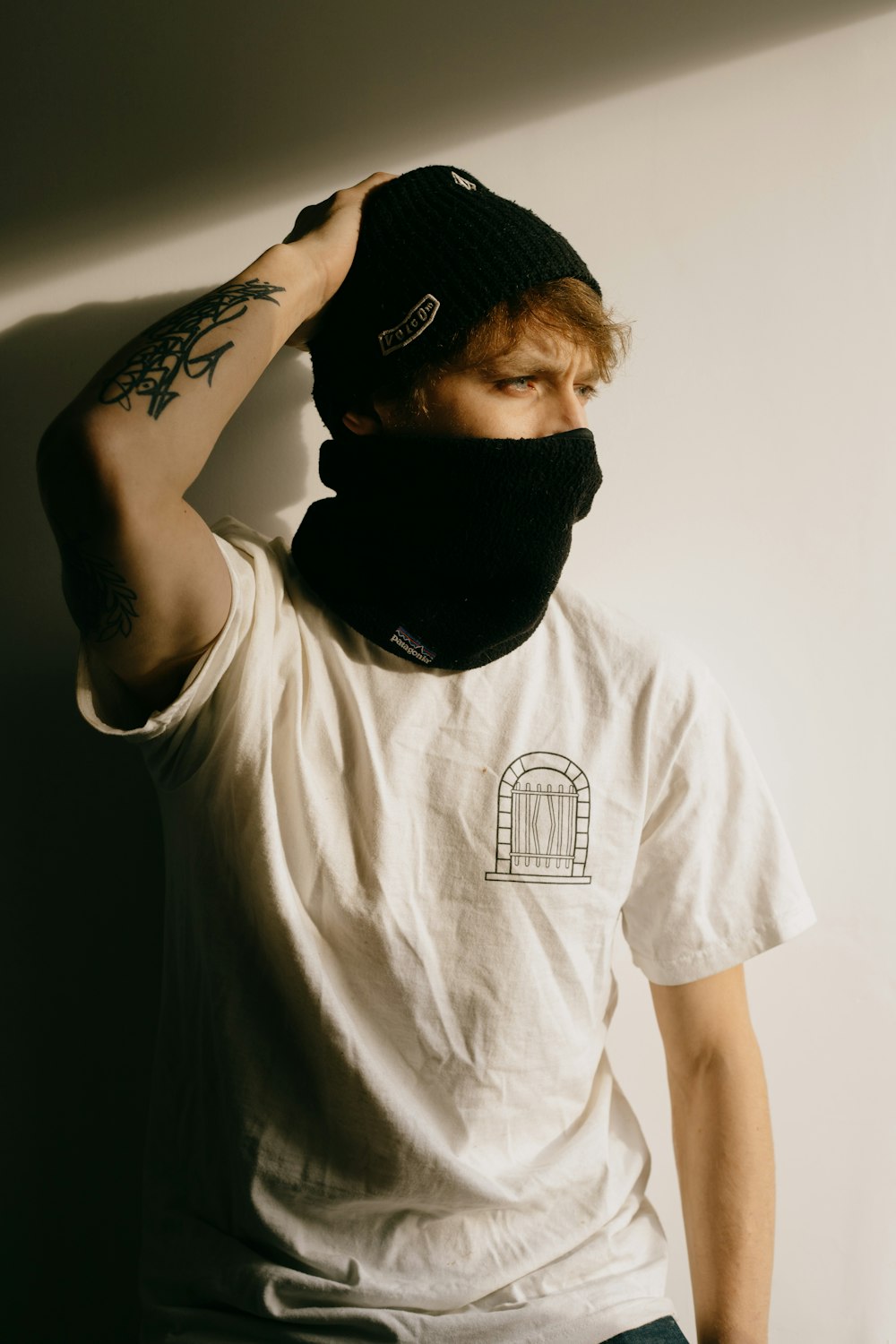 Hombre con camiseta blanca de cuello redondo que cubre la cara con gorro de punto negro