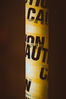 Yellow caution tape wrapped around an object, set against a dark background.