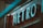 Large metallic letters spelling 'METRO' are prominently displayed with a teal lighting effect. The sign appears to be mounted on a red background, suggesting the entrance to a subway or a transportation hub. There's a blurred element in the foreground, adding depth to the image.