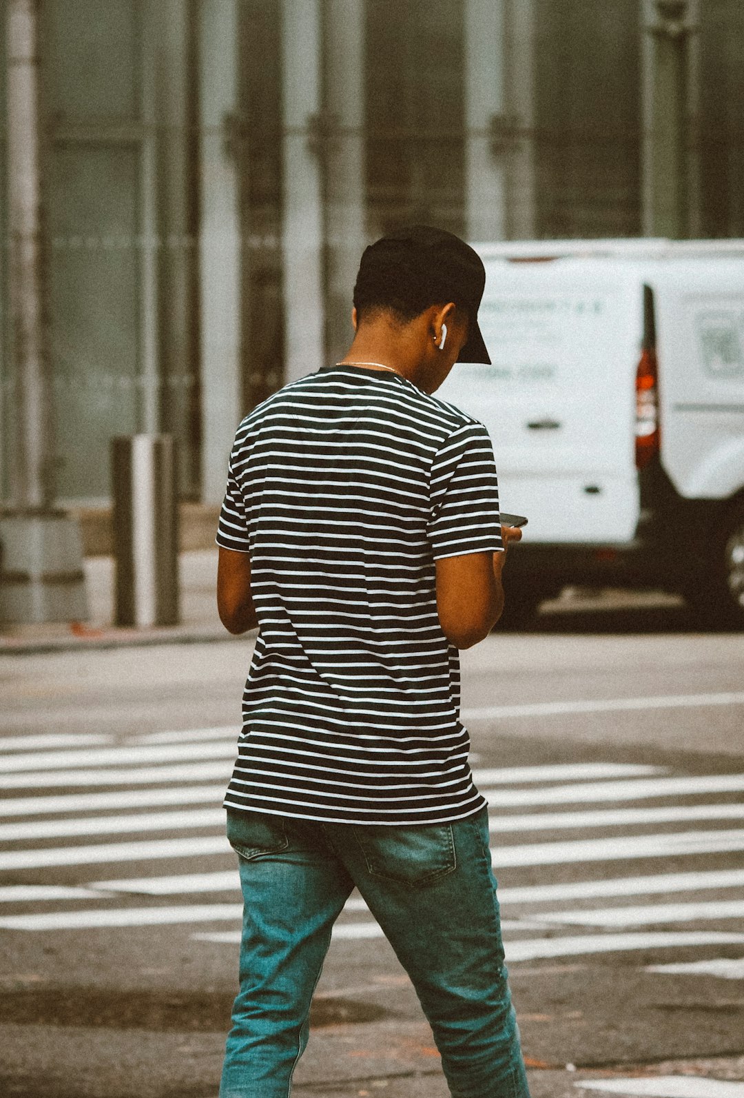 man in black and white striped shirt and blue denim jeans standing on sidewalk during daytime