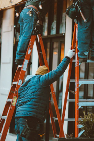 person in blue bubble jacket and brown knit cap standing on red ladder