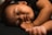 A peaceful baby is sleeping with eyes closed and a calm expression. The child is lying on a dark surface, with one arm resting near the face. The lighting is soft, highlighting the gentle features and serene atmosphere.