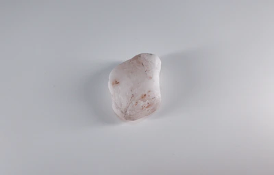 A smooth, pale beige stone resting gently on soft linen fabric under warm natural light.