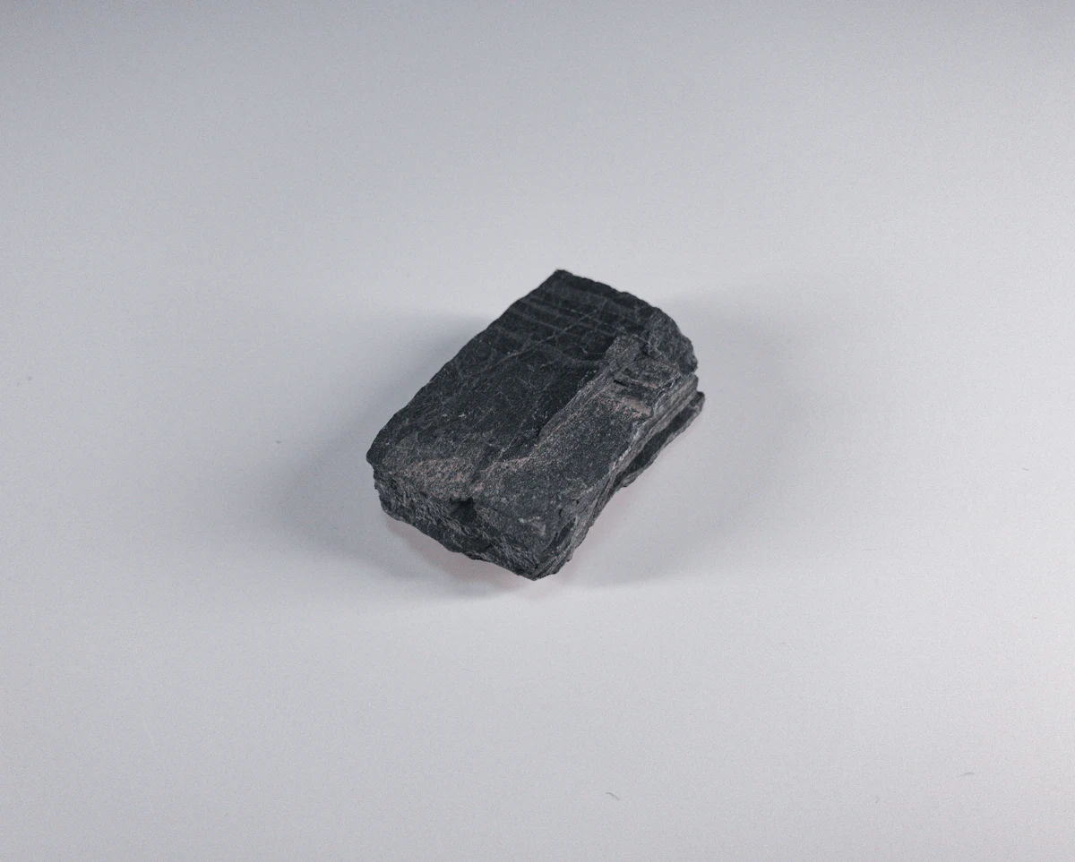 A hand holding a fragment of black tourmaline crystal against a pale background, showing the dense, opaque character of the threshold stone