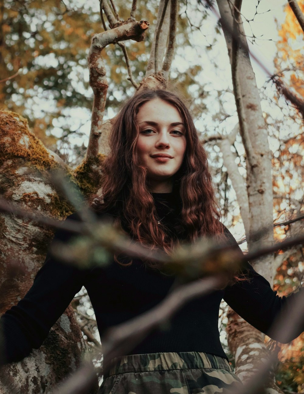 Femme en chemise à manches longues à fleurs noires et blanches debout à côté d’un arbre brun