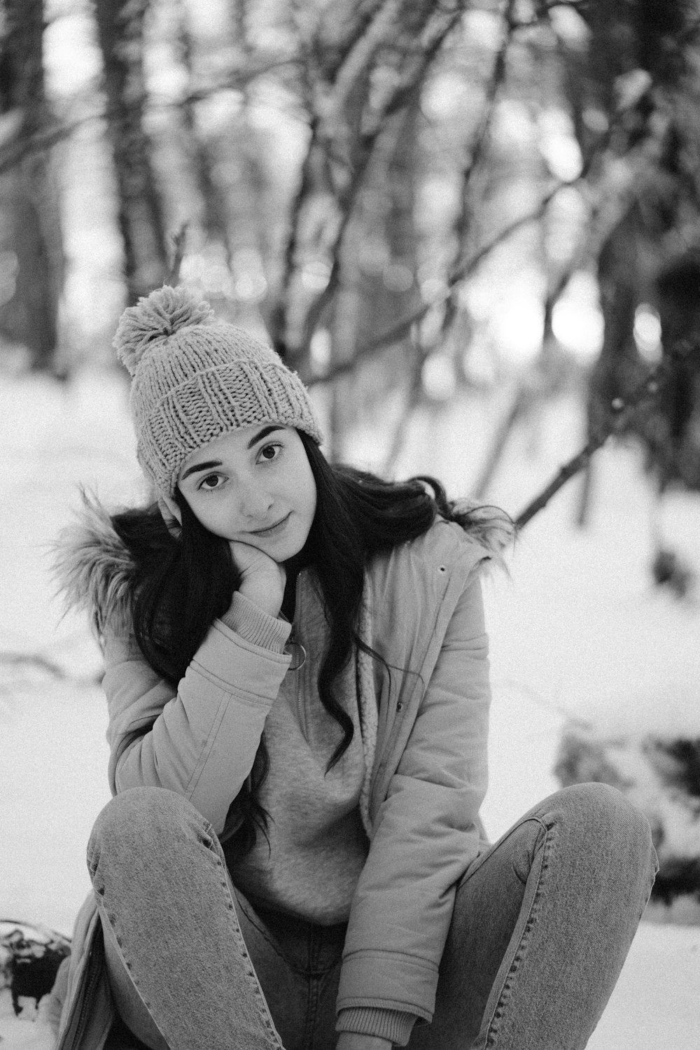 grayscale photo of woman in knit cap and jacket sitting on snow covered ground