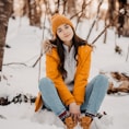 woman in blue jacket and blue denim jeans sitting on snow covered ground during daytime