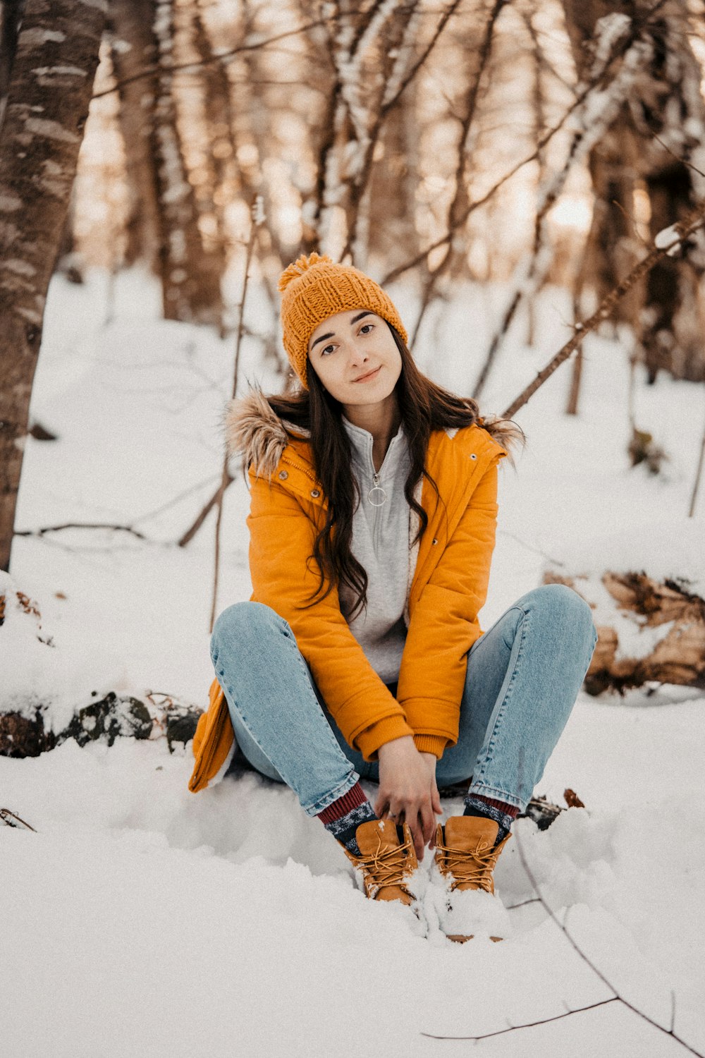 woman in blue jacket and blue denim jeans sitting on snow covered ground during daytime