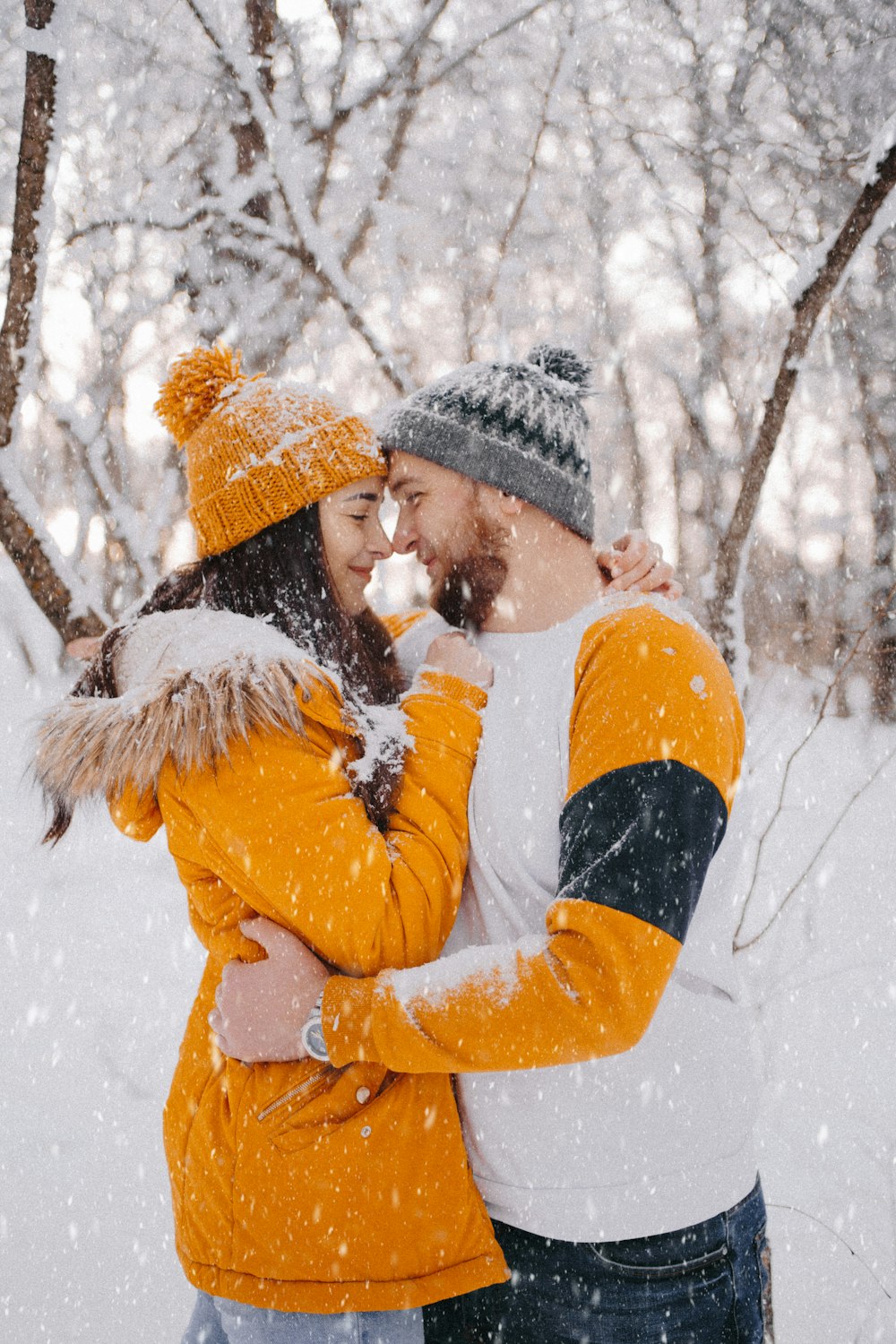woman in yellow jacket and black knit cap kissing man in black jacket
