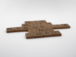 Wooden Scrabble tiles arranged on a white surface forming the words 'HOPE', 'MEMORIES', 'AND', 'WITH', and 'DIE' in a crossword style.