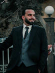 man in black suit jacket standing near black metal fence during daytime