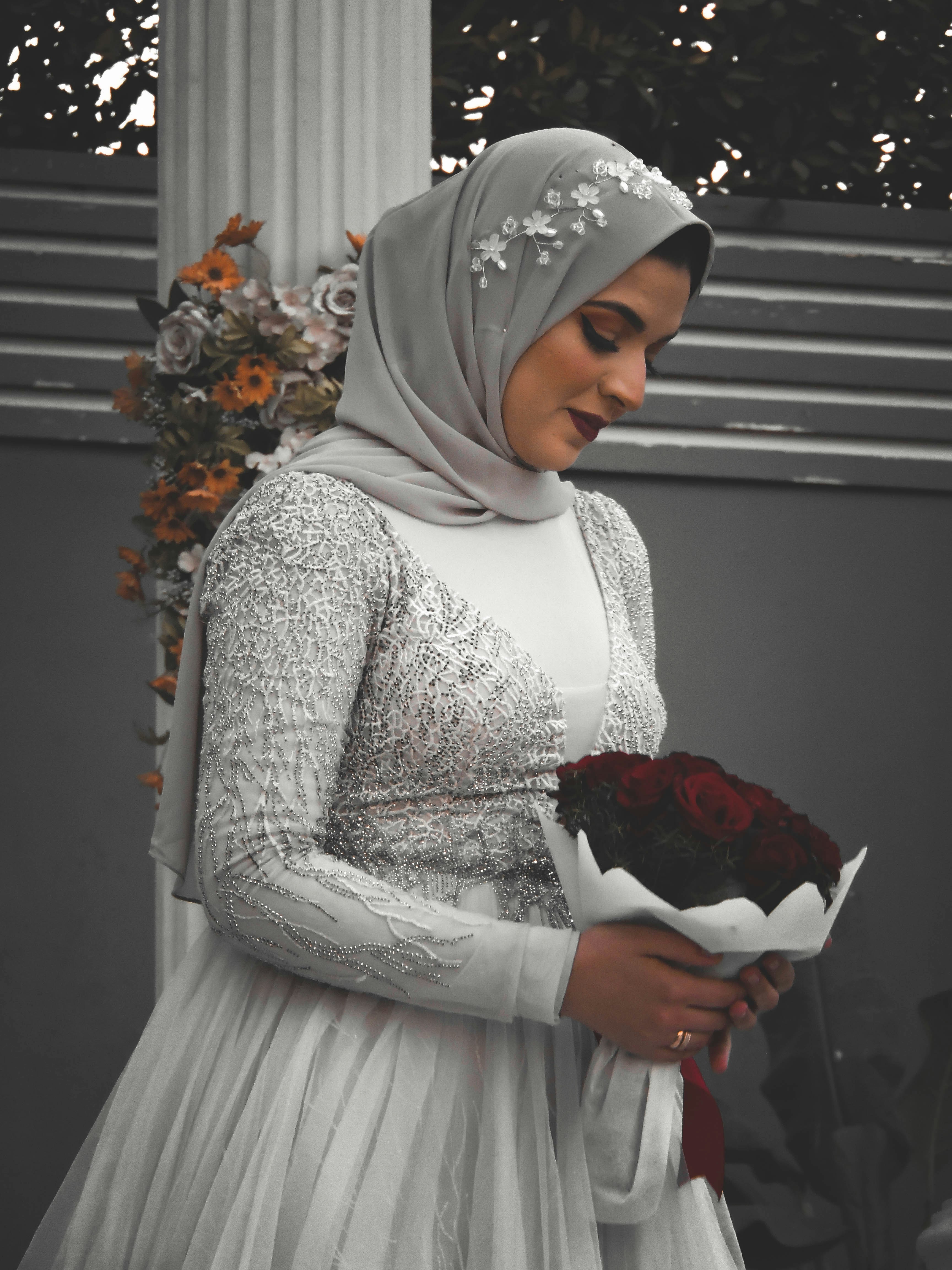woman in white hijab holding red bouquet