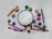 An arrangement of colorful embroidery thread skeins encircles a circular embroidery hoop with a white cloth. The threads are in various shades including pink, purple, green, orange, and blue. Several bobbins of thread are visible, as well as two embroidery needles placed on the cloth within the hoop.