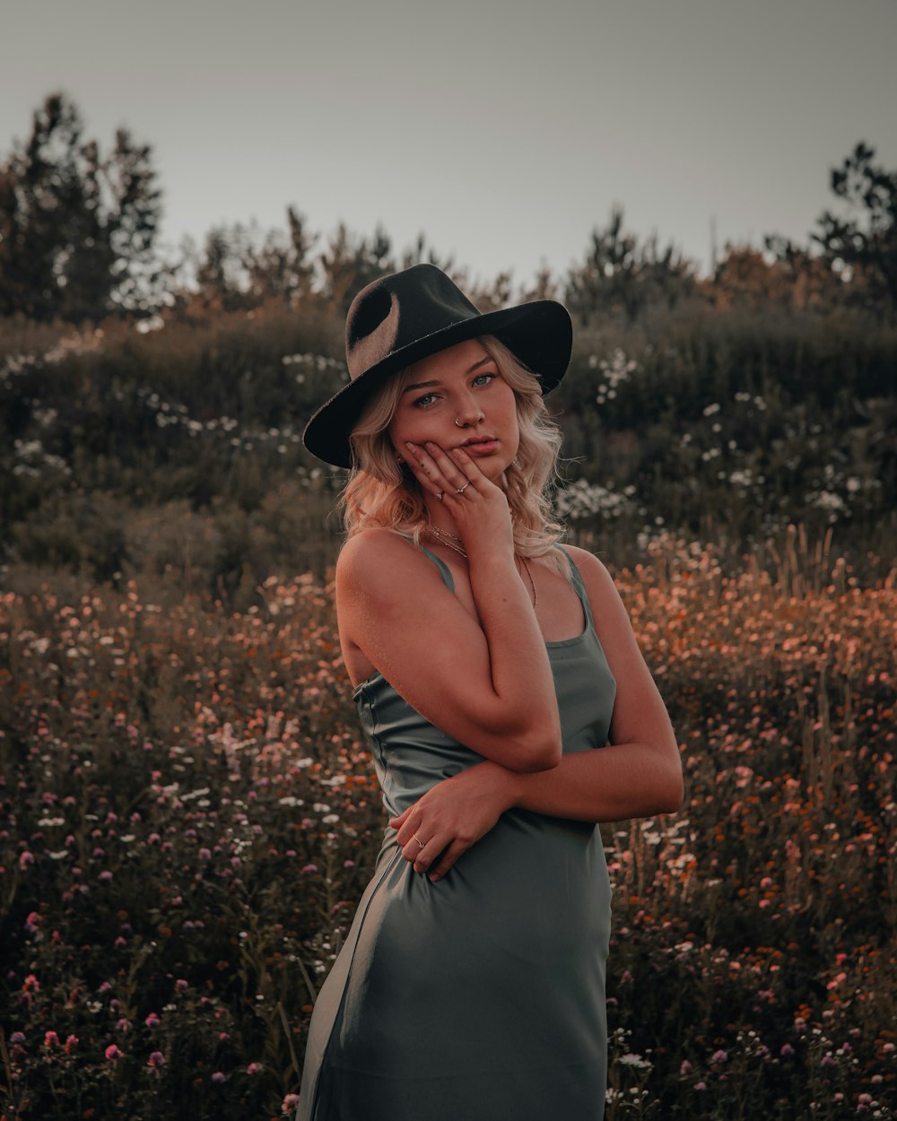 woman in white tank dress wearing black hat standing on red flower field during daytime