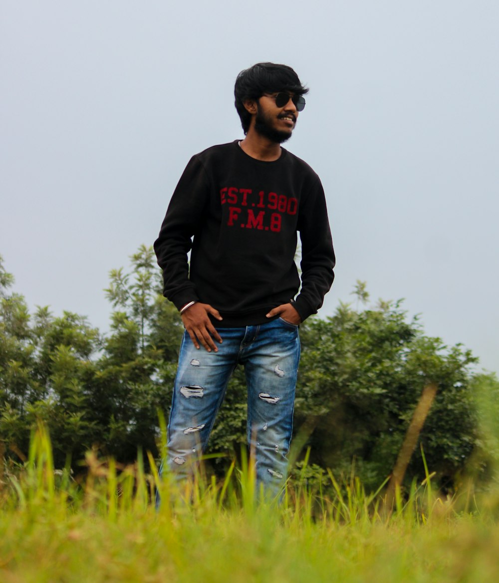 man in black sweater and blue denim jeans standing on green grass field during daytime