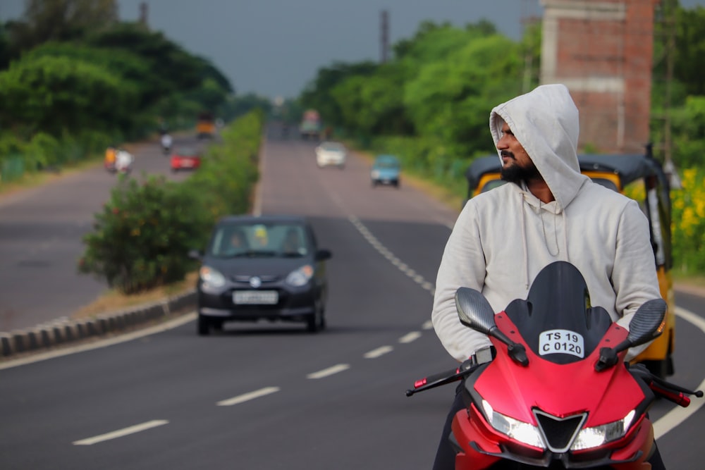 man in white hoodie riding red motorcycle on road during daytime