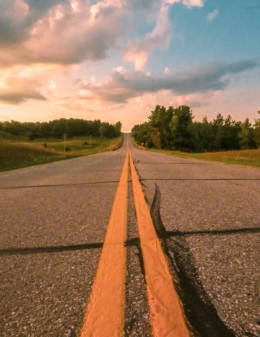 gray concrete road between green grass field under white clouds during daytime