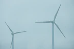 Two large wind turbines with three blades each stand against a cloudy blue sky, indicating a focus on renewable energy.