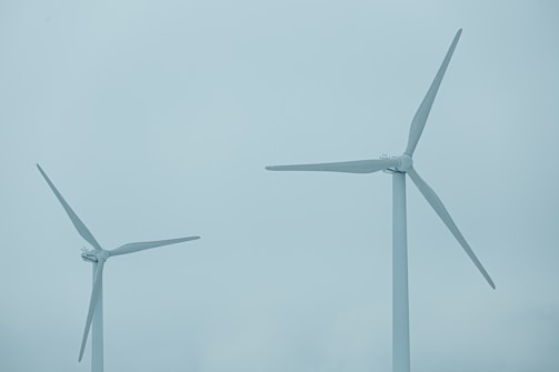 Two large wind turbines with three blades each stand against a cloudy blue sky, indicating a focus on renewable energy.