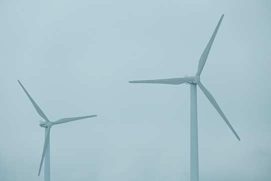 Two large wind turbines with three blades each stand against a cloudy blue sky, indicating a focus on renewable energy.