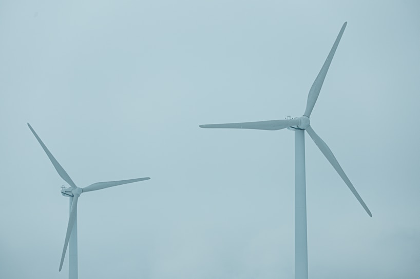 Two large wind turbines with three blades each stand against a cloudy blue sky, indicating a focus on renewable energy.