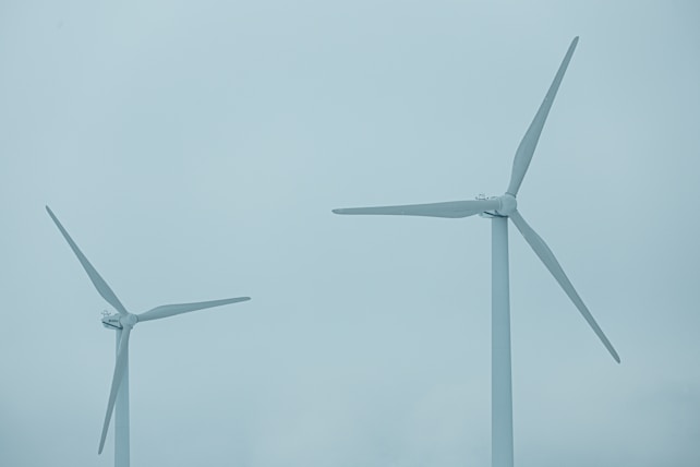 Two large wind turbines with three blades each stand against a cloudy blue sky, indicating a focus on renewable energy.