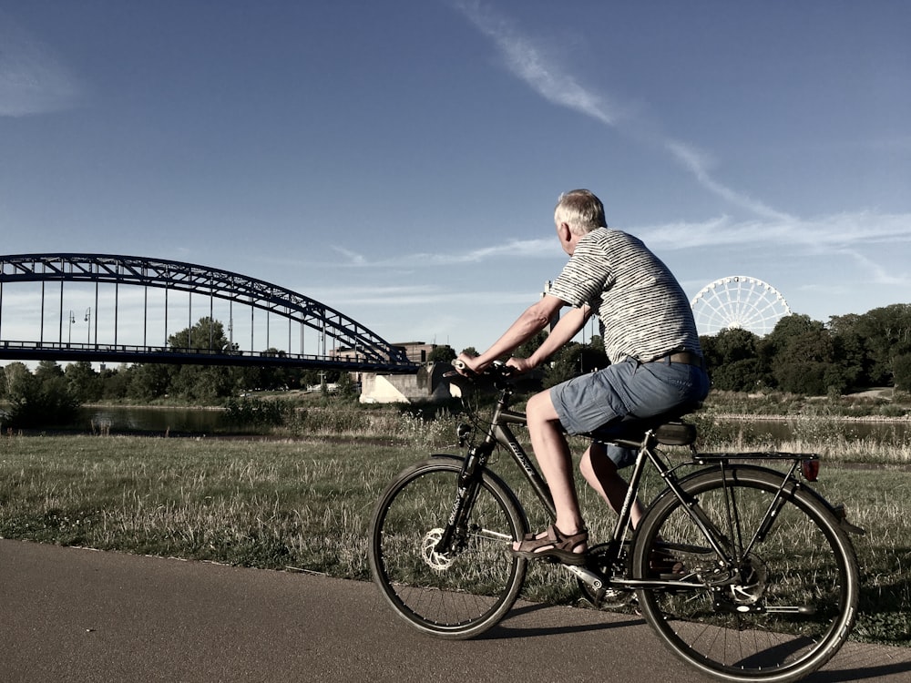 Hombre con camisa a rayas grises y blancas montando bicicleta negra en la carretera durante el día