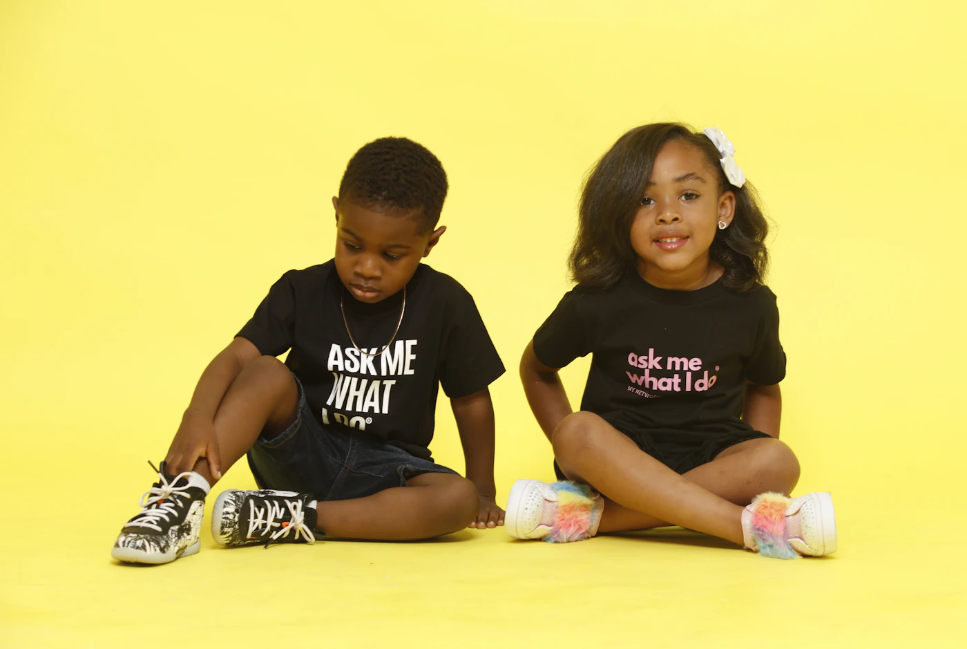 Two kids in black tees against a yellow wall