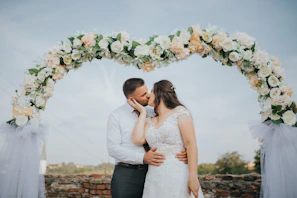 A bride and groom sharing a joyful kiss under a blooming archway at sunset.