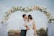 A joyful couple sharing a kiss under a floral arch during their wedding ceremony.