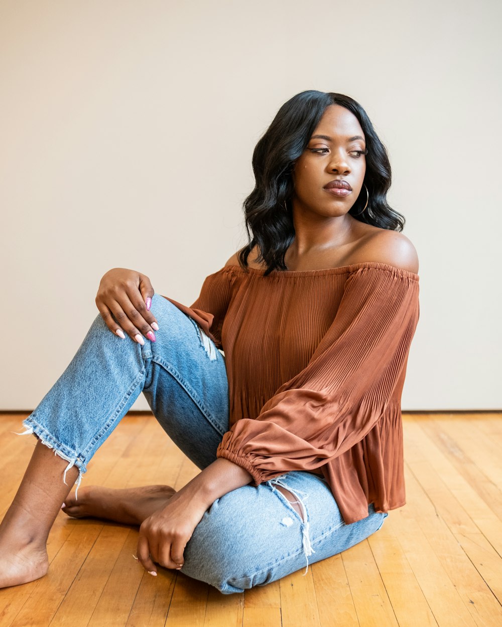 woman in brown long sleeve shirt and blue denim jeans sitting on brown wooden floor