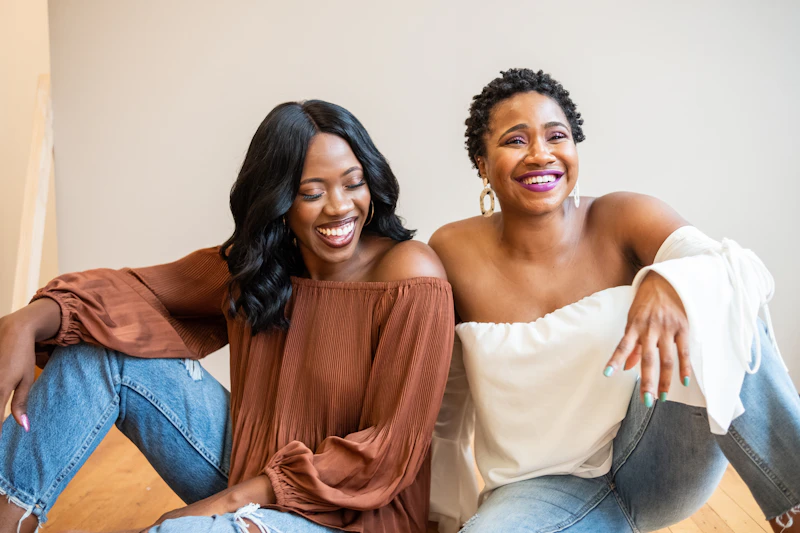 Two Black women sitting close together outdoors, laughing warmly