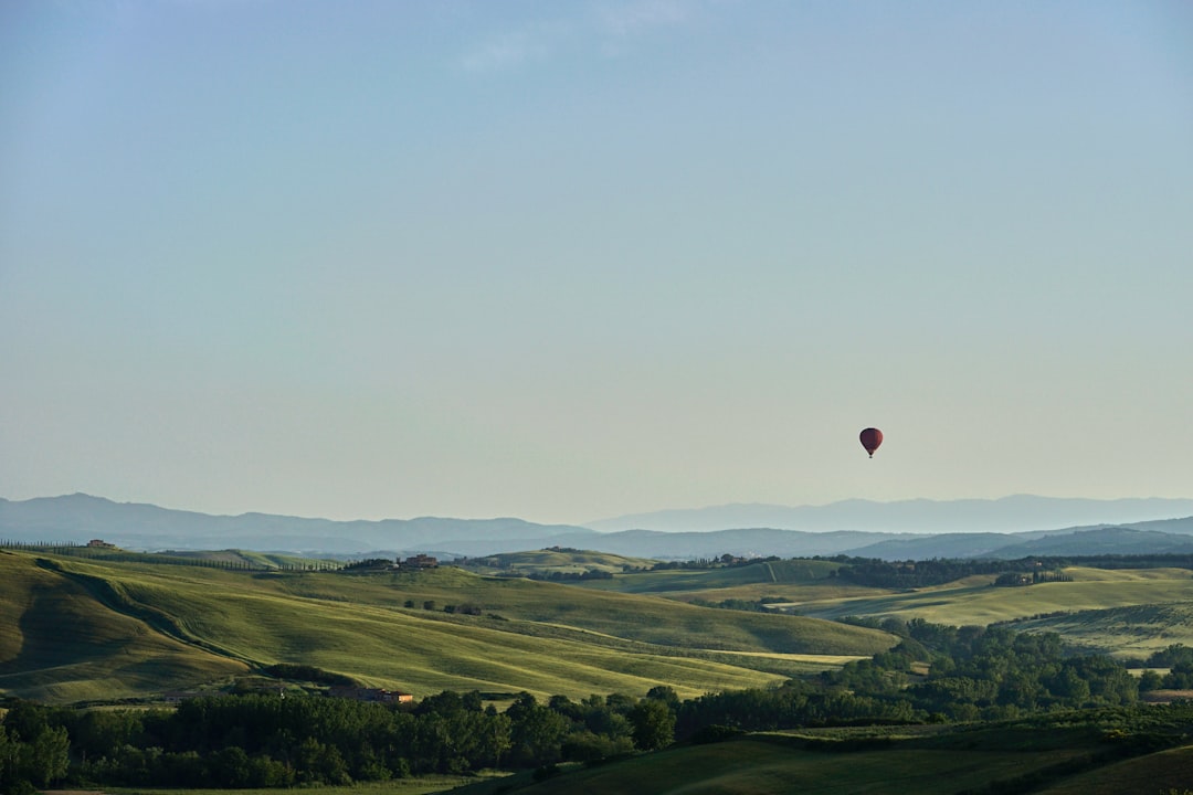 red hot air balloon flying over green grass field during daytime