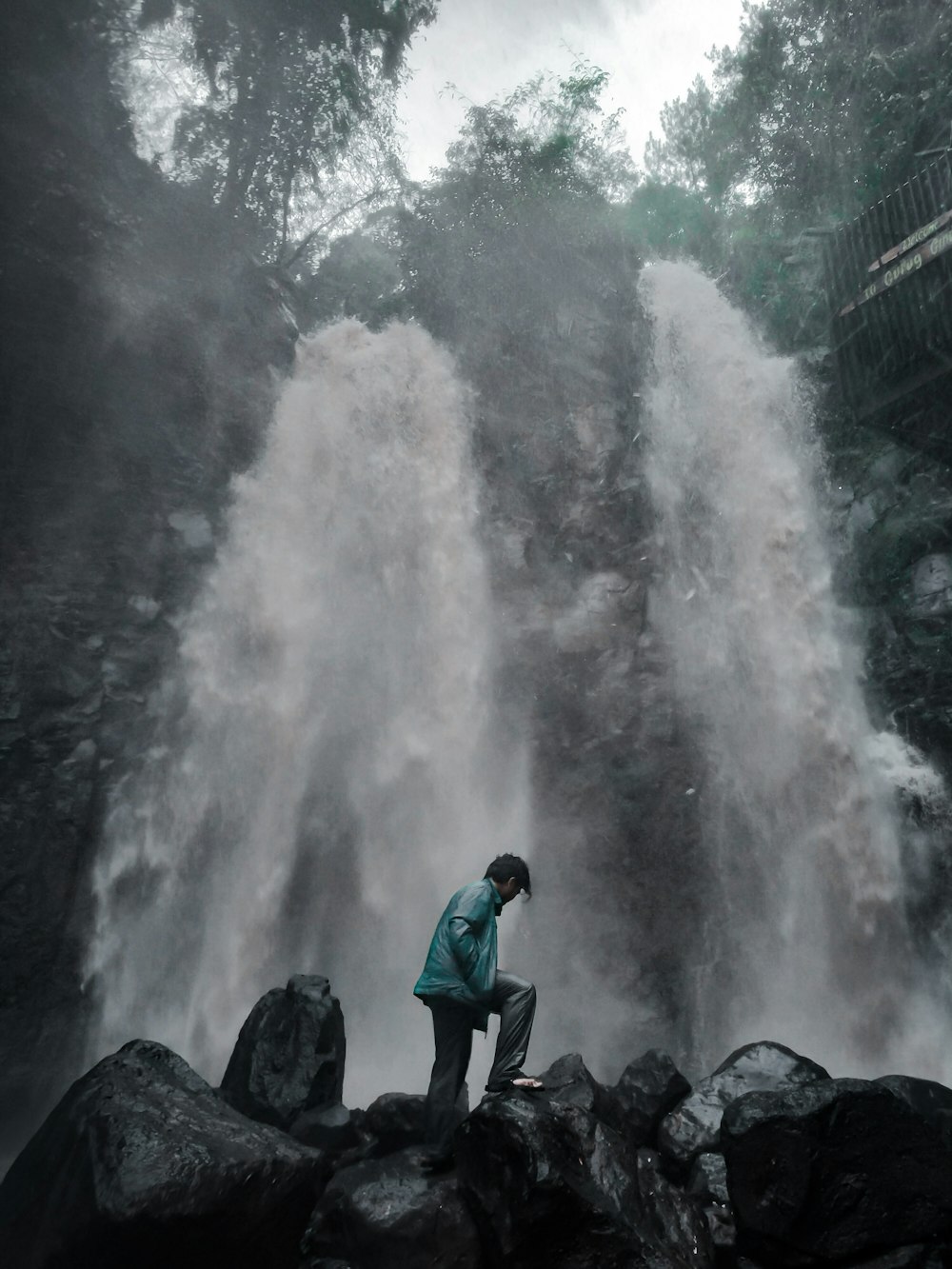 homme en veste bleue debout sur le rocher près des chutes d’eau pendant la journée