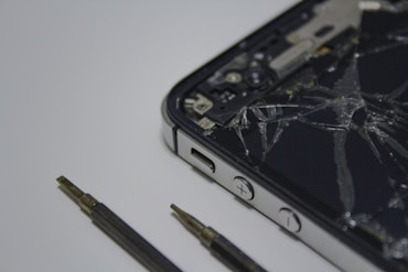 Close-up of a technician carefully replacing a cracked smartphone screen with precision tools on a workbench.