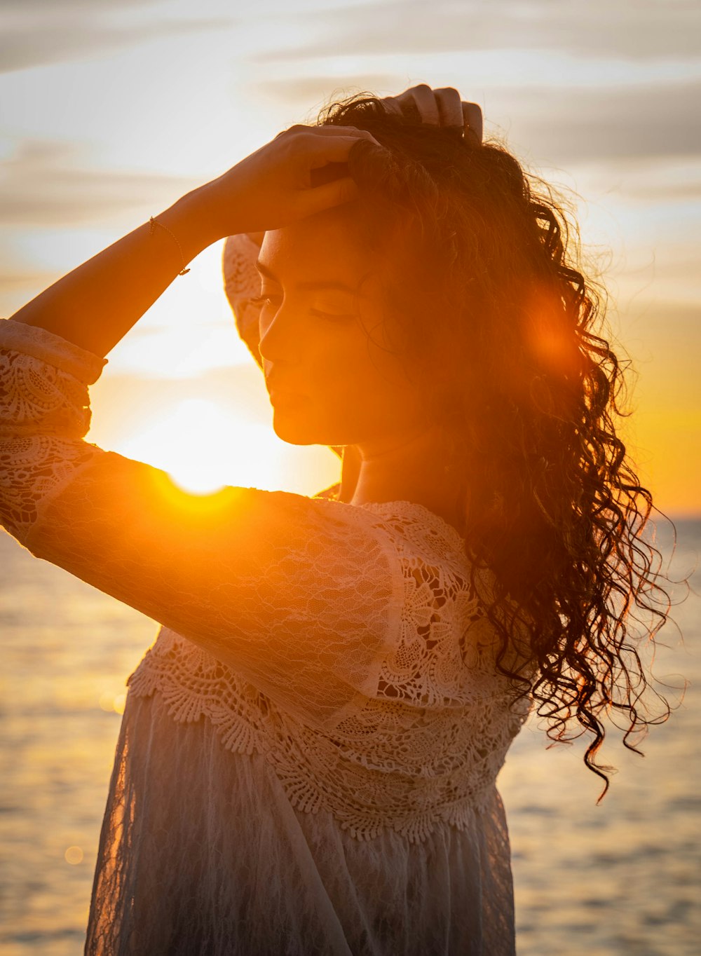 donna in abito di pizzo bianco che tiene i capelli durante il tramonto