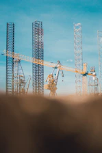 A bustling construction site with cranes lifting steel beams against a clear blue sky.
