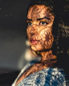 A close-up of a woman's eyes behind a delicate black lace mask, illuminated by soft golden light.