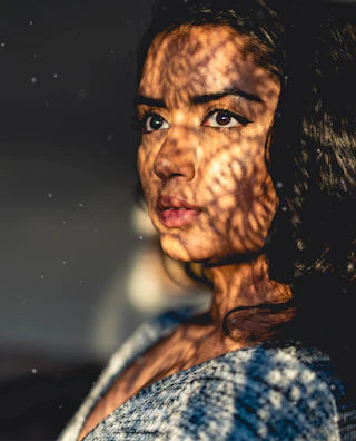 A close-up of a woman's eyes behind a delicate black lace mask, illuminated by soft golden light.