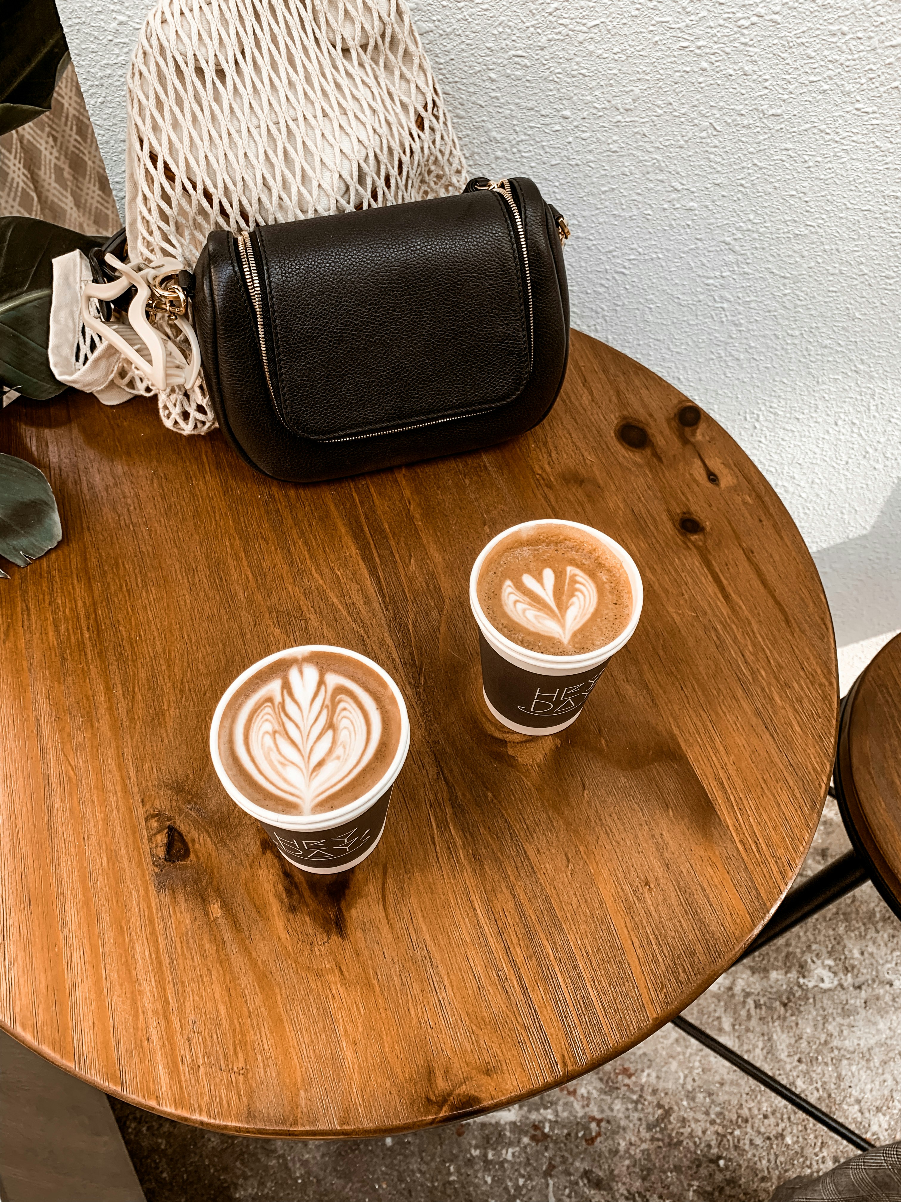 black leather bag beside cappuccino in white ceramic mug on brown wooden table