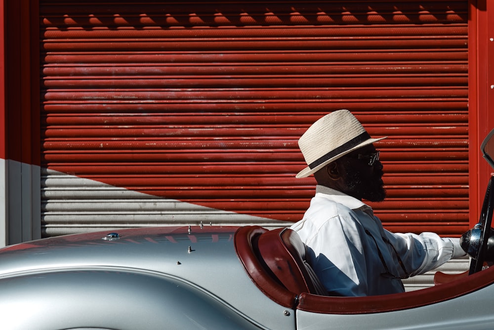 man in white dress shirt wearing brown fedora hat sitting on white car