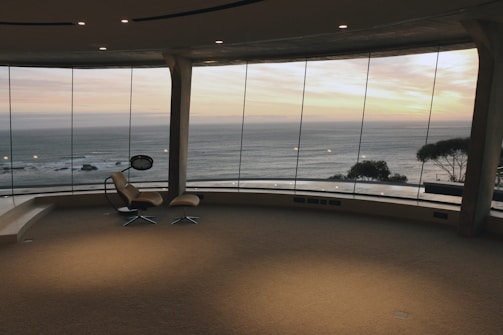 Modern beachfront hotel room with balcony overlooking the sea at sunset.