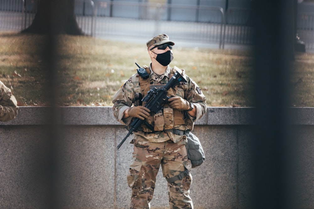 Hombre con uniforme de camuflaje marrón y negro sosteniendo un rifle