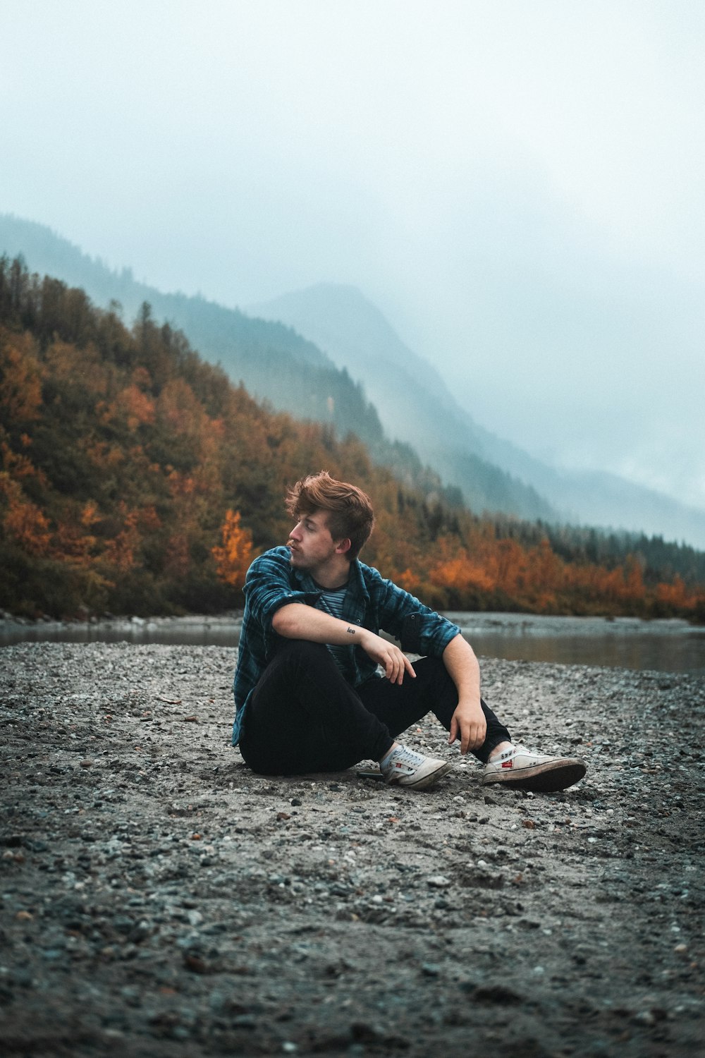 woman in blue jacket and black pants sitting on gray rock near river during daytime