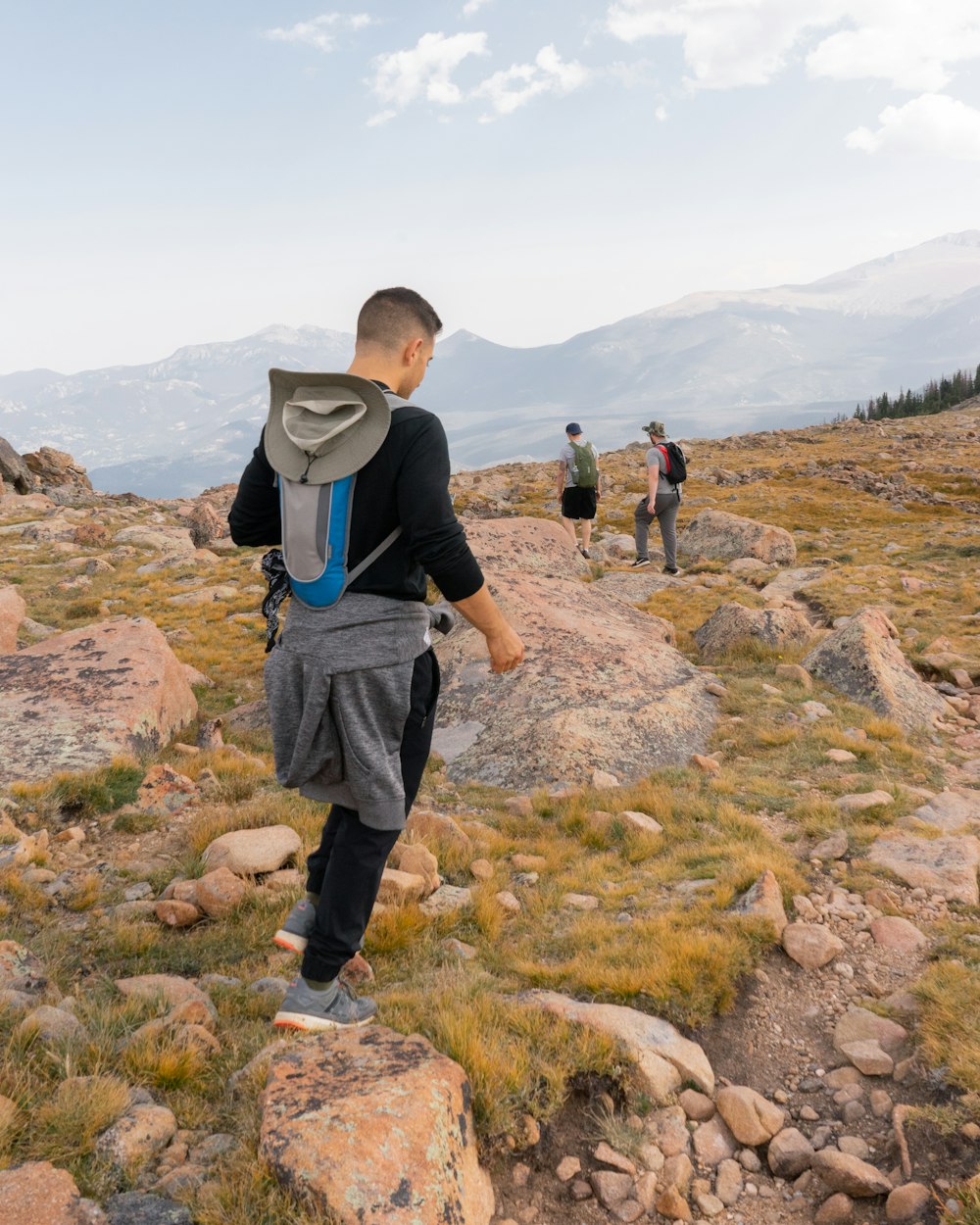 man in blue t-shirt and black pants carrying backpack standing on rock during daytime