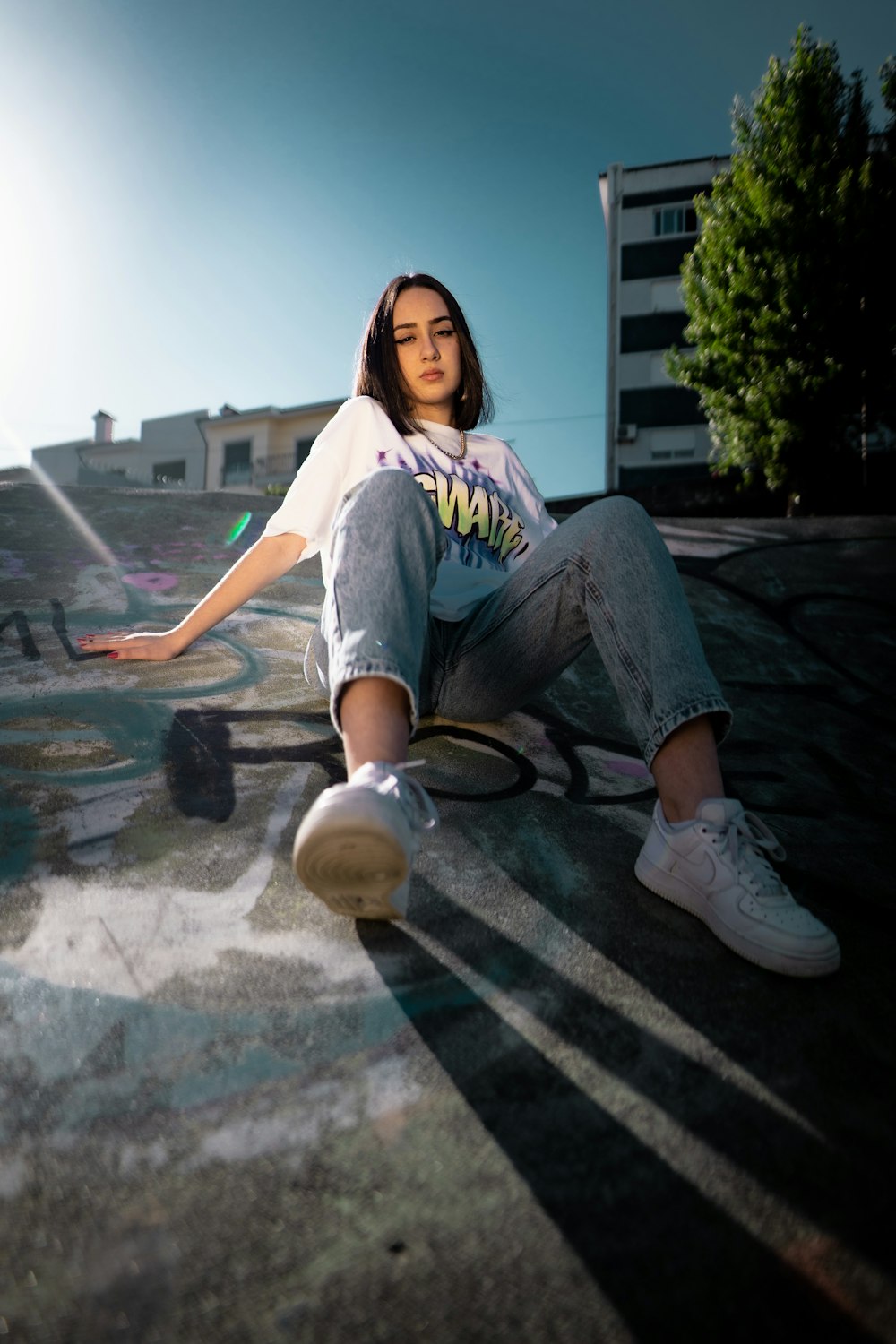 woman in white shirt and blue denim jeans sitting on concrete floor